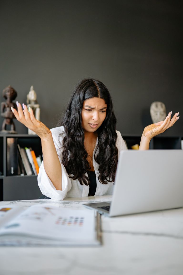 A frustrated businesswoman sits at her office desk, puzzled over her laptop.